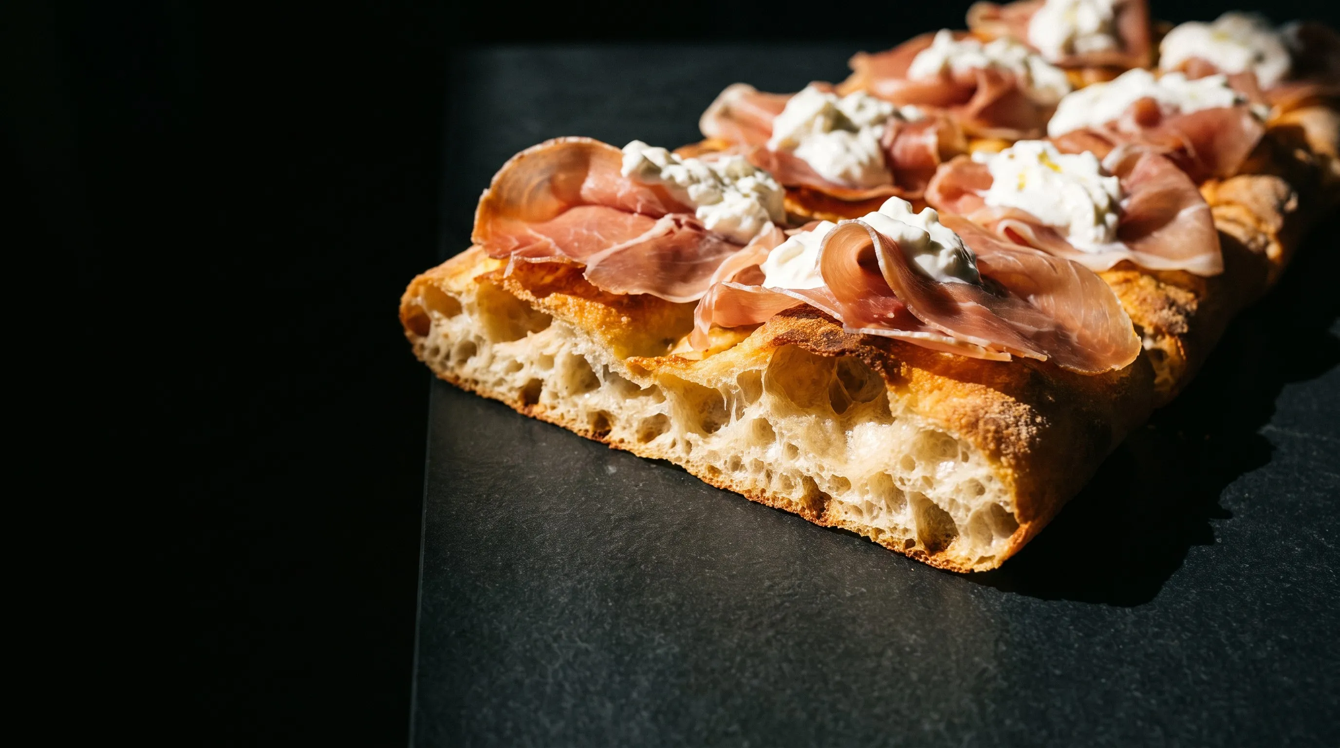 A long rectangular pizza al taglio cut to show an open, airy crumb.